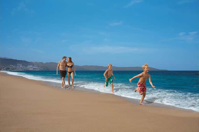 Family playing in ocean surf with sandy beach and distant coastline