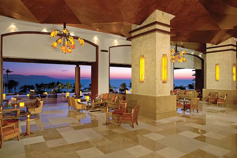 Elegant lobby lounge at sunset with ocean views, modern chandeliers, and warm lighting