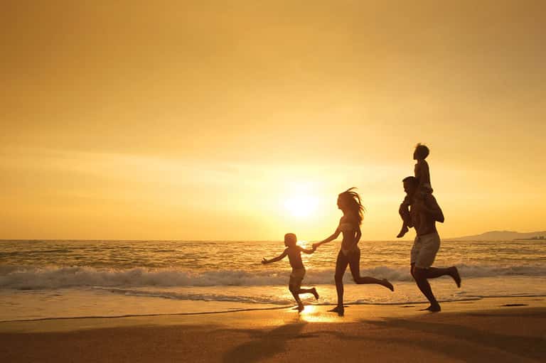 Family running on beach at sunset with golden light reflecting on water