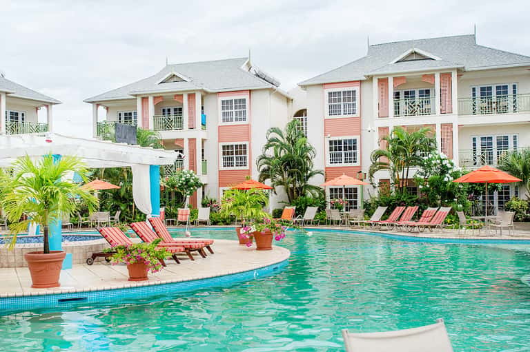 Colorful Caribbean-style resort with coral buildings, pool, and palm trees