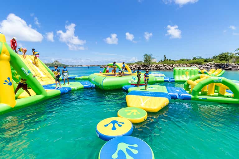 Inflatable water park with green and yellow obstacle course structures in bright turquoise tropical waters