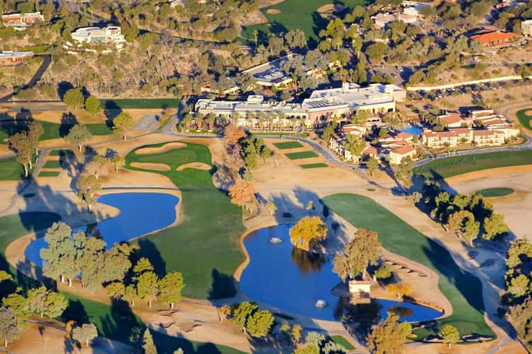 Aerial view of luxury resort with golf course, main building, water features, and surrounding grounds