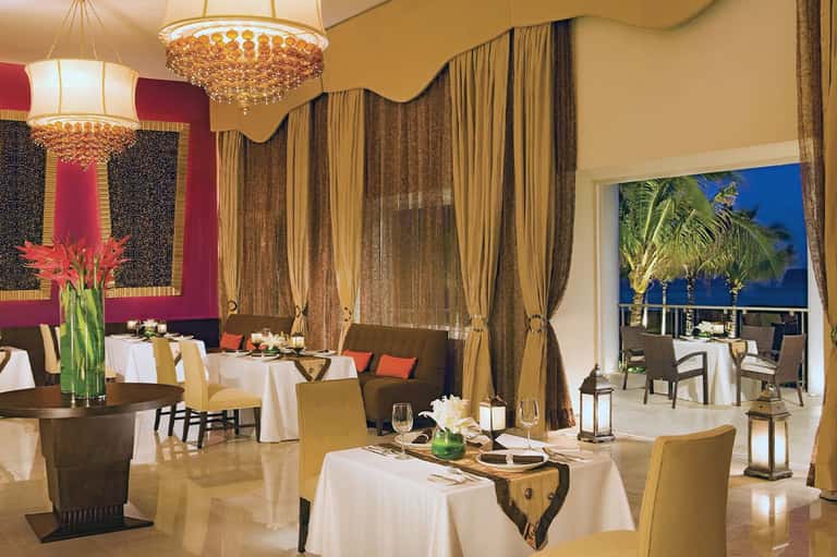Elegant fine dining restaurant with gold chandeliers, draped curtains, and ocean views