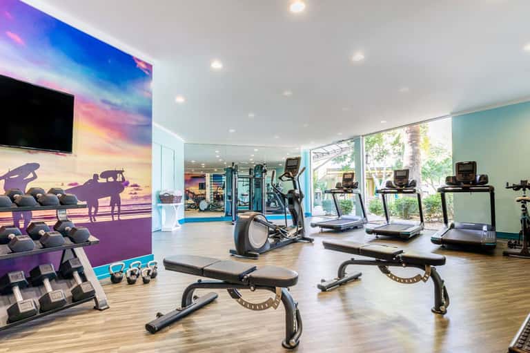 Modern fitness center with colorful wall mural of surfer, treadmills, exercise bikes, and dumbbell weights