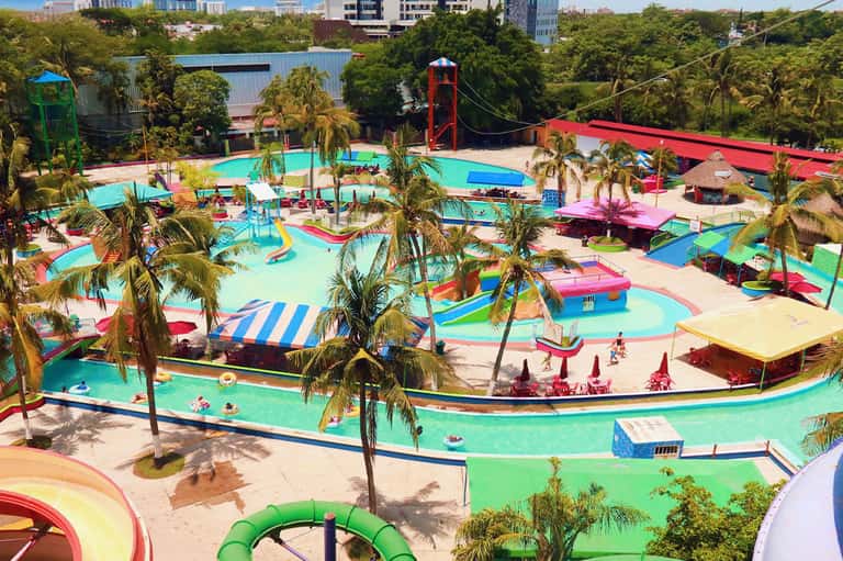 Colorful lazy river water park with vibrant pink, blue, and green pools, slides, and palm trees