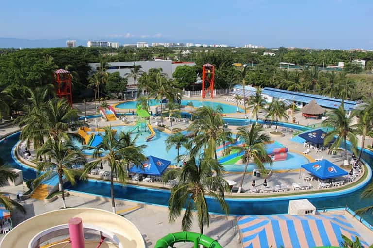Aerial view of large water park with multiple pools, slides, and palm trees among landscaping