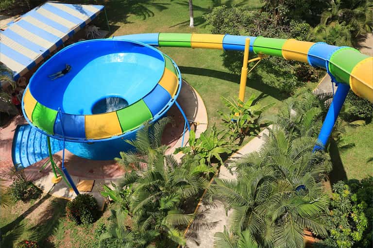 Colorful water slide and trampoline in resort pool surrounded by green lawn and palm trees