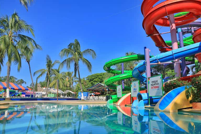 Colorful water park with red and green spiral slides, palm trees, and clear blue pool in sunny setting