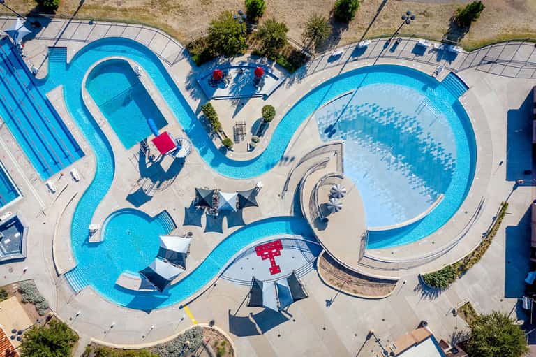 Aerial view of curved swimming pools and water park with umbrellas and landscaping