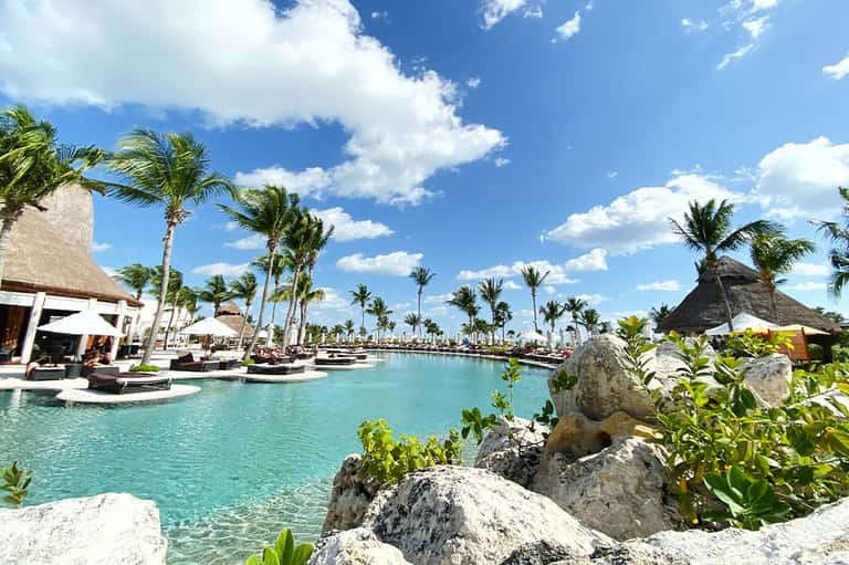 Turquoise lagoon pool with thatched-roof structures and palm trees in tropical resort setting