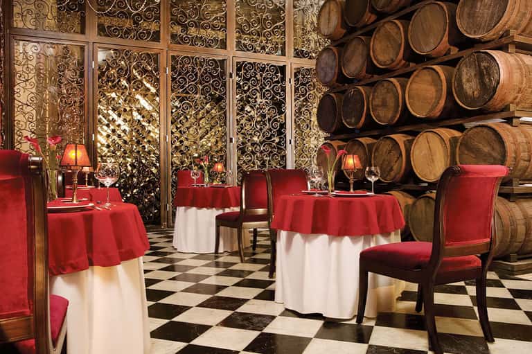 Elegant dining room with red tablecloths, ornate gold screens, and wine barrel display