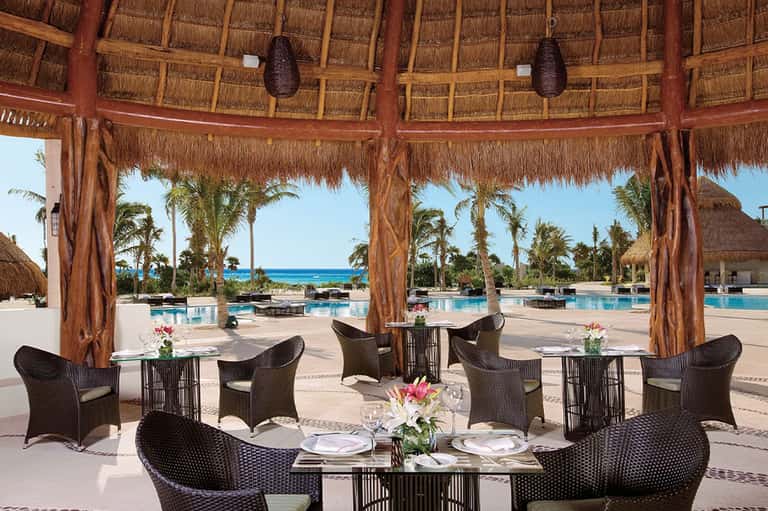 Thatched gazebo dining area with wicker chairs overlooking pool and palm landscape