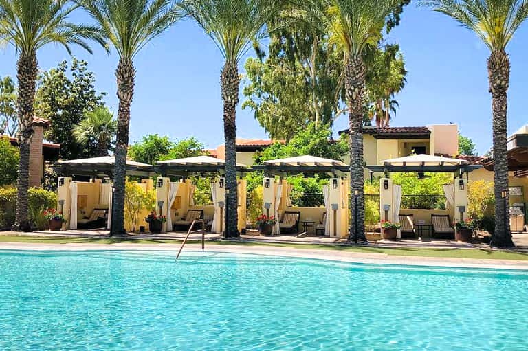 Luxury resort pool with crystal-clear turquoise water, palm trees, and cream-colored cabanas with white umbrellas