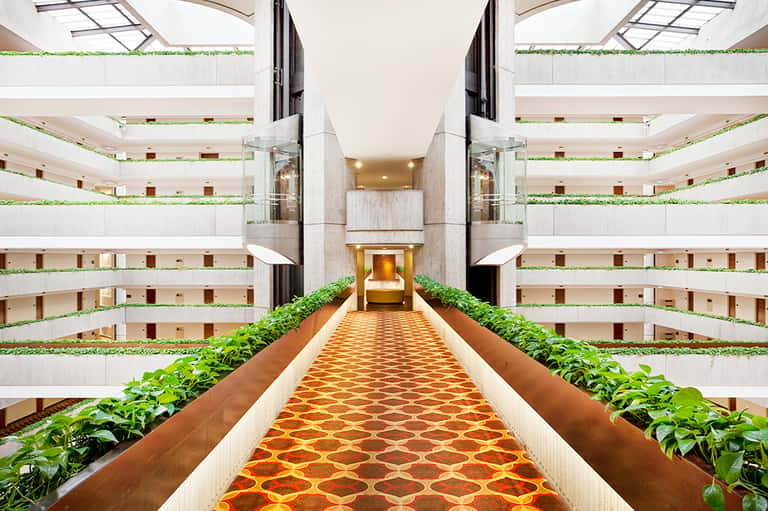 Hotel atrium with symmetrical balconies, indoor garden, and patterned carpet