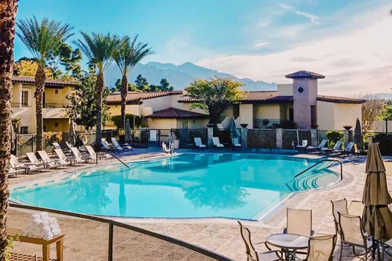 Resort pool with palm trees, lounge chairs, and mountain views in the background