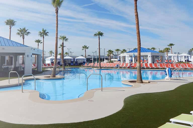 Modern resort pool with palm trees, lounge chairs, and white cabanas under blue sky