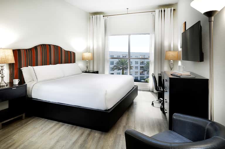 Contemporary hotel bedroom with striped headboard, white bedding, ocean view balcony, and flat-screen TV