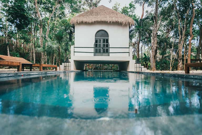 Modern pool with white building and thatched roof reflected in turquoise water