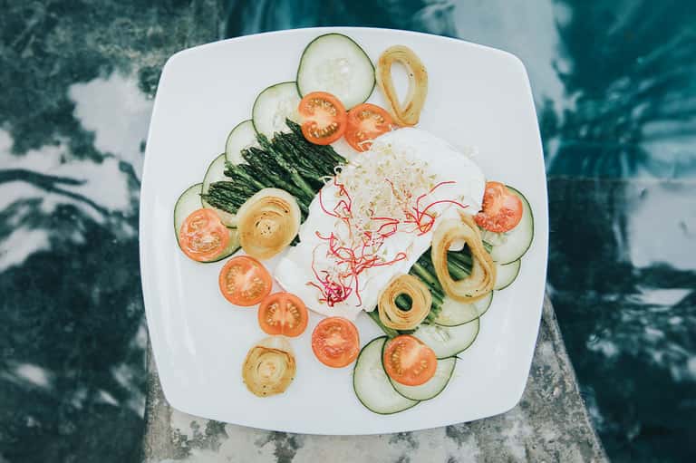 Elegantly plated salad with cucumber, tomato, and crispy onion rings on white plate
