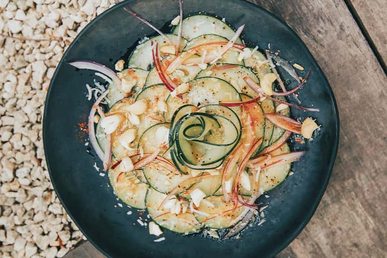 Gourmet plated noodle dish with zucchini spirals, shrimp, and garnishes on dark slate plate