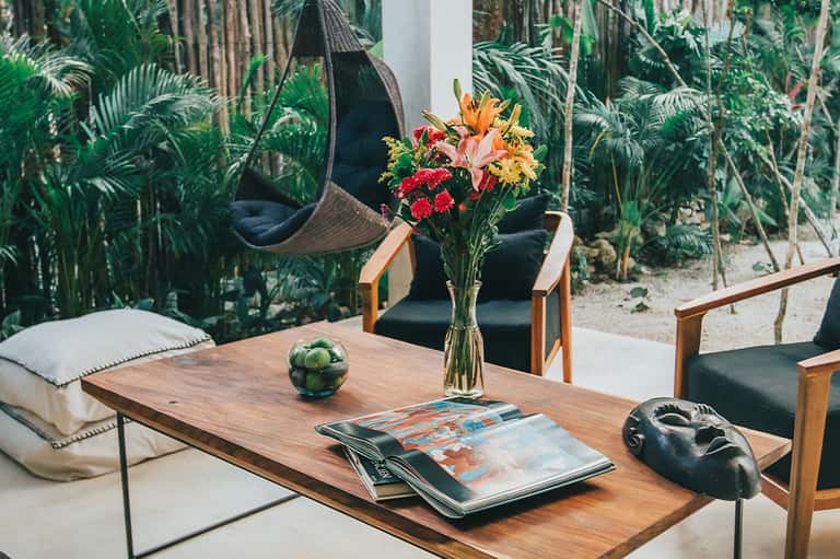 Tropical garden seating area with wooden table, fresh flowers, and hanging hammock