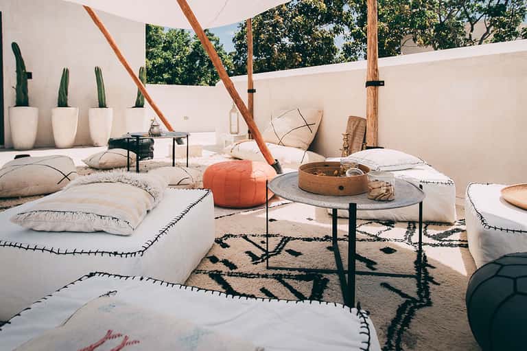 Minimalist rooftop lounge with floor cushions, fire pit, and white walls