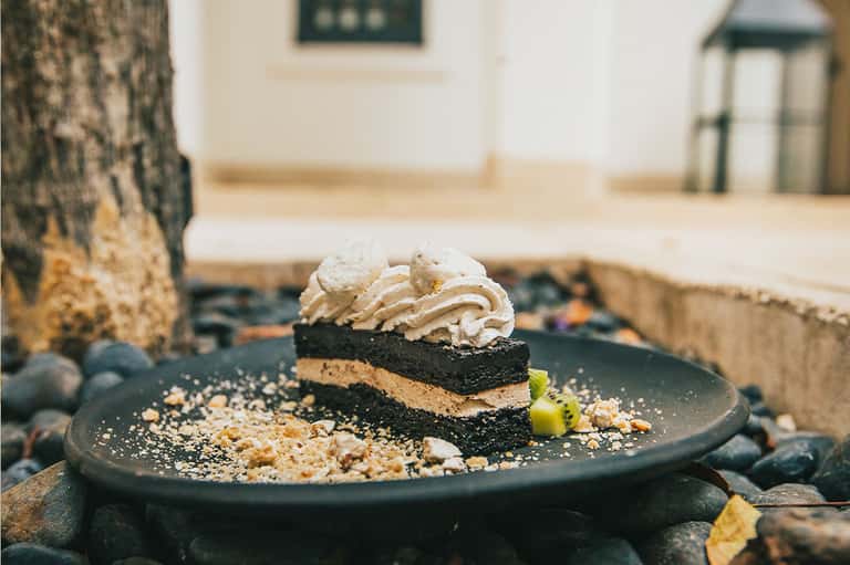 Gourmet dessert plate with layered chocolate cake and whipped cream on dark plate outdoors