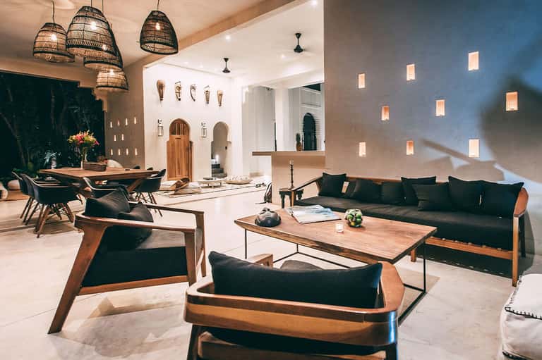 Modern resort courtyard with woven pendant lights, dark furniture, white walls, and geometric skylights