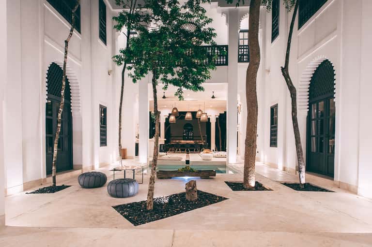 Modern courtyard with white arches, green doors, and tree-lined seating area