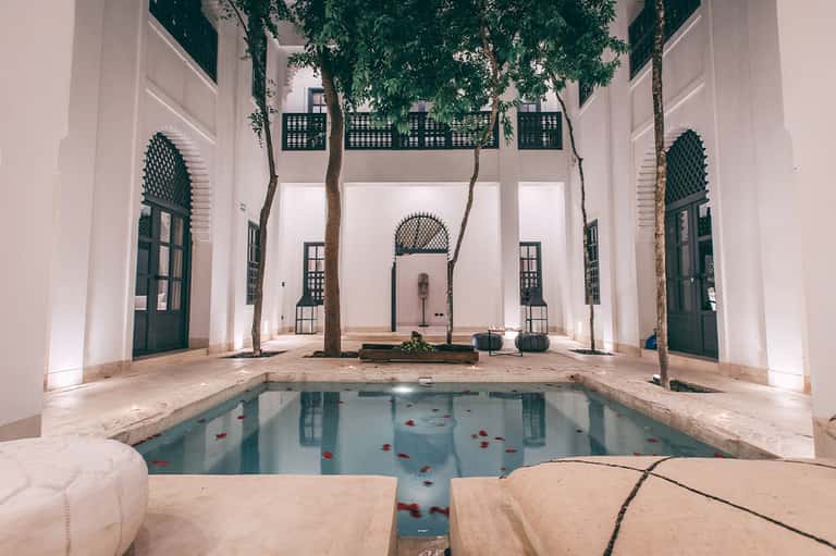 Minimalist courtyard with central pool, white walls, arched doorways, and tall trees