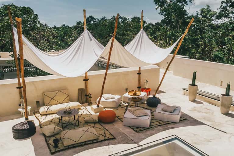 Rooftop lounge area with white draped canopies, cushioned seating, and scenic green surroundings