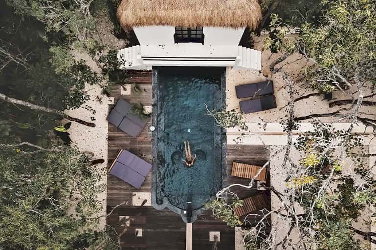 Aerial view of luxury resort bungalow with thatched roof, private pool, and jungle surroundings