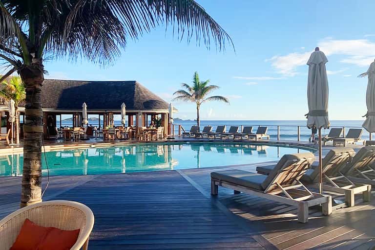 Luxury beachfront resort pool with tiki bar, ocean view, and palm trees at sunset
