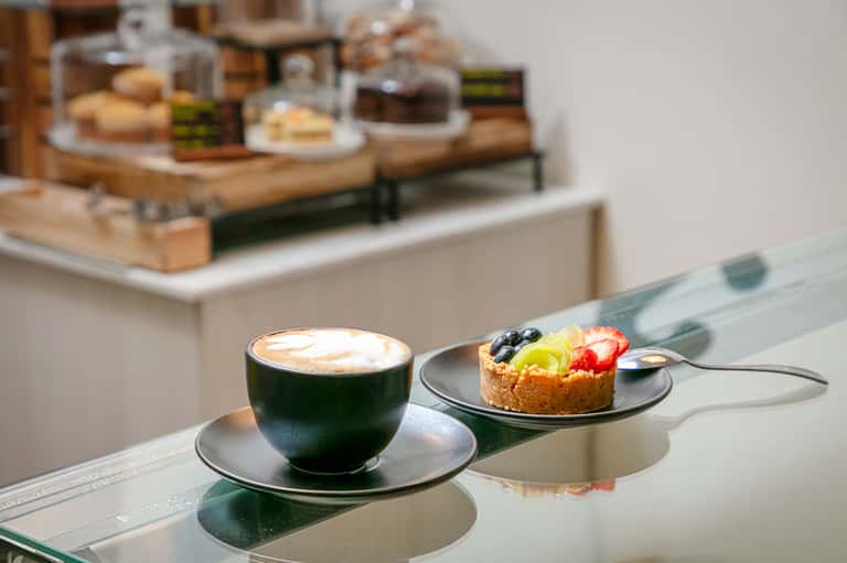 Latte coffee and fruit pastry on modern white counter with bakery display in background