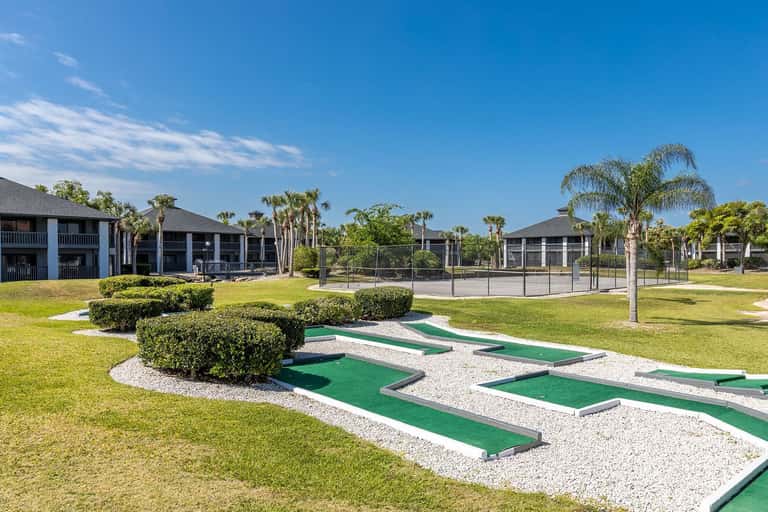 Mini golf course on resort grounds with palm trees, manicured grass, and hotel buildings