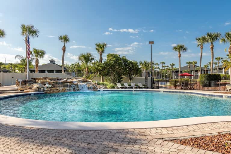 Lagoon-style pool with rock waterfall feature, surrounded by palm trees and manicured grounds