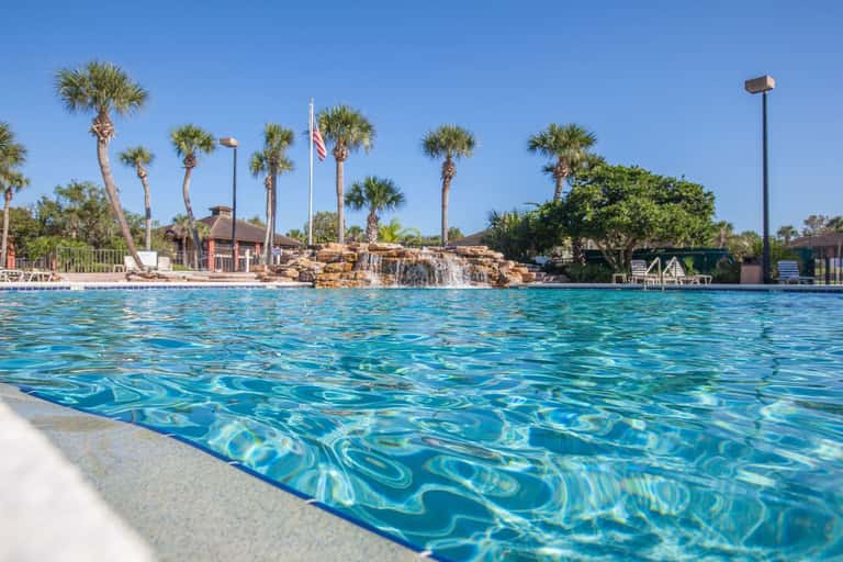 Resort pool with waterfall feature, palm trees, and lounging area in daylight