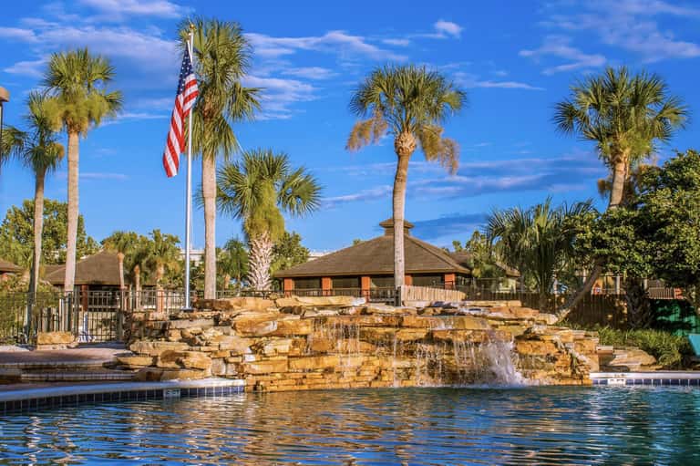 Resort pool with stone waterfall feature, palm trees, and covered pavilions