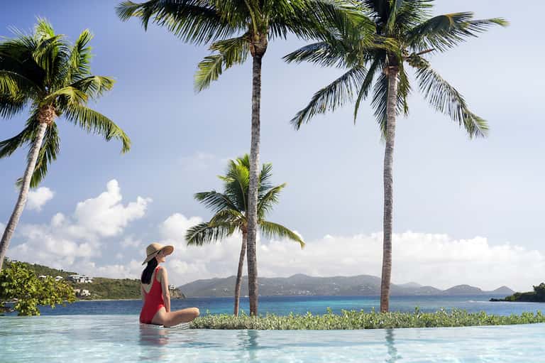 Woman in red dress relaxing in infinity pool with palm trees and tropical ocean view