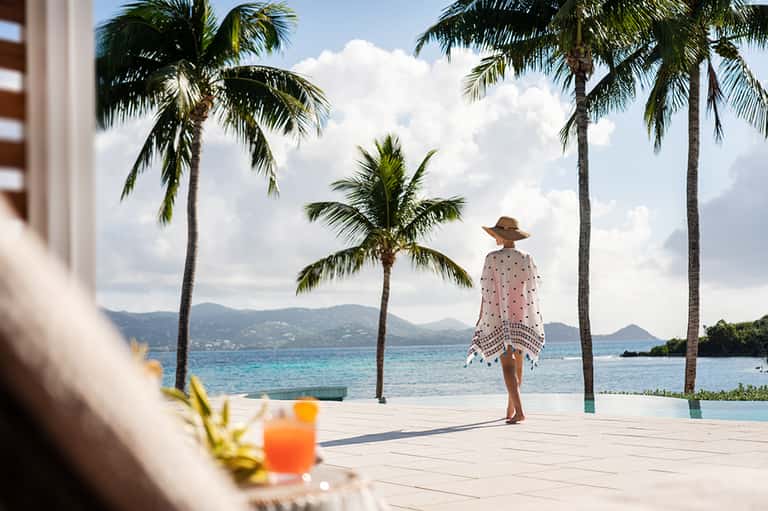 Woman in beachwear standing on wooden deck facing tropical ocean and palm trees