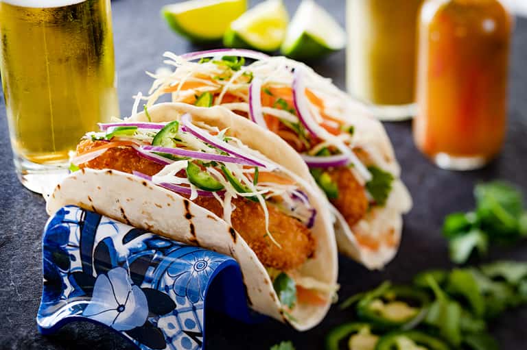 Gourmet fish tacos with fresh toppings served with beer and lime wedges