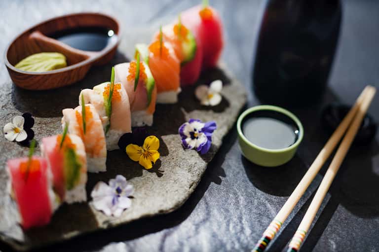 Artfully arranged sushi rolls with edible flowers and condiments on stone slate