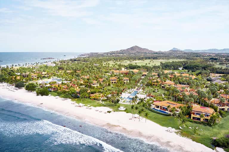 Aerial view of beachfront resort with colorful villas, palm trees, and white sand beach