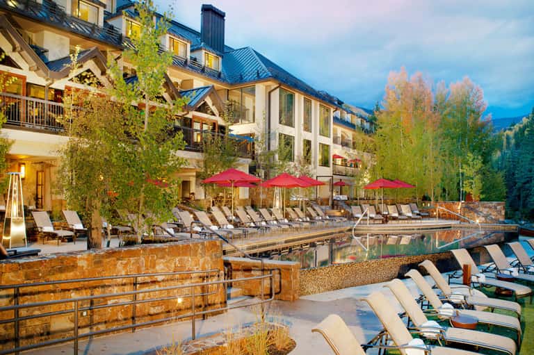 Luxury mountain resort with heated pool, red umbrellas, lounge chairs, and snow-capped peaks in background