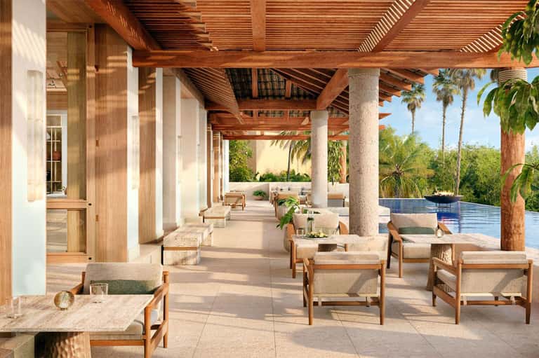 Modern poolside lounge area with wooden pergola, comfortable seating, and infinity pool overlooking tropical landscape