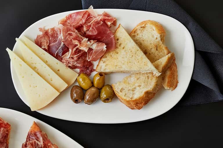 Appetizer plate with cured meats, cheese, olives, and toasted bread slices