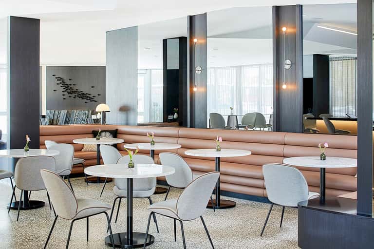 Modern hotel lounge with pink seating, mirrors, and white round tables