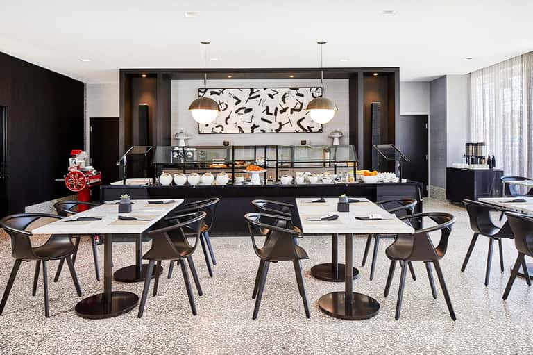 Modern hotel dining area with black tables, chairs, pendant lights and service counter with pastries