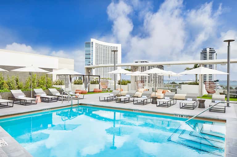 Modern rooftop pool deck with white umbrellas, lounge chairs, and city skyline views