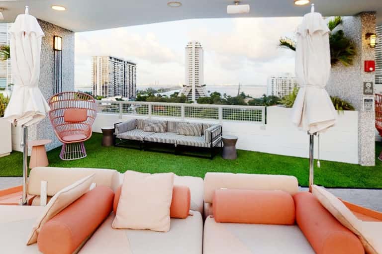 Modern rooftop lounge with city views, orange seating, white umbrellas, and artificial grass